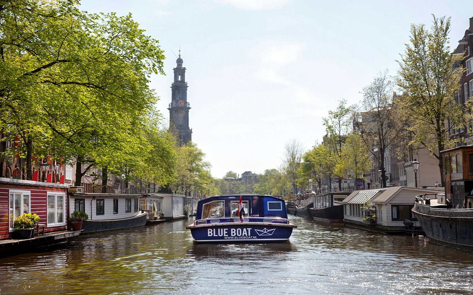 Blue boat cruising Amsterdam canal with Westerkerk tower in view.