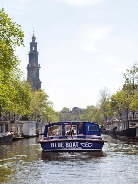 Blue boat cruising Amsterdam canal with Westerkerk tower in view.