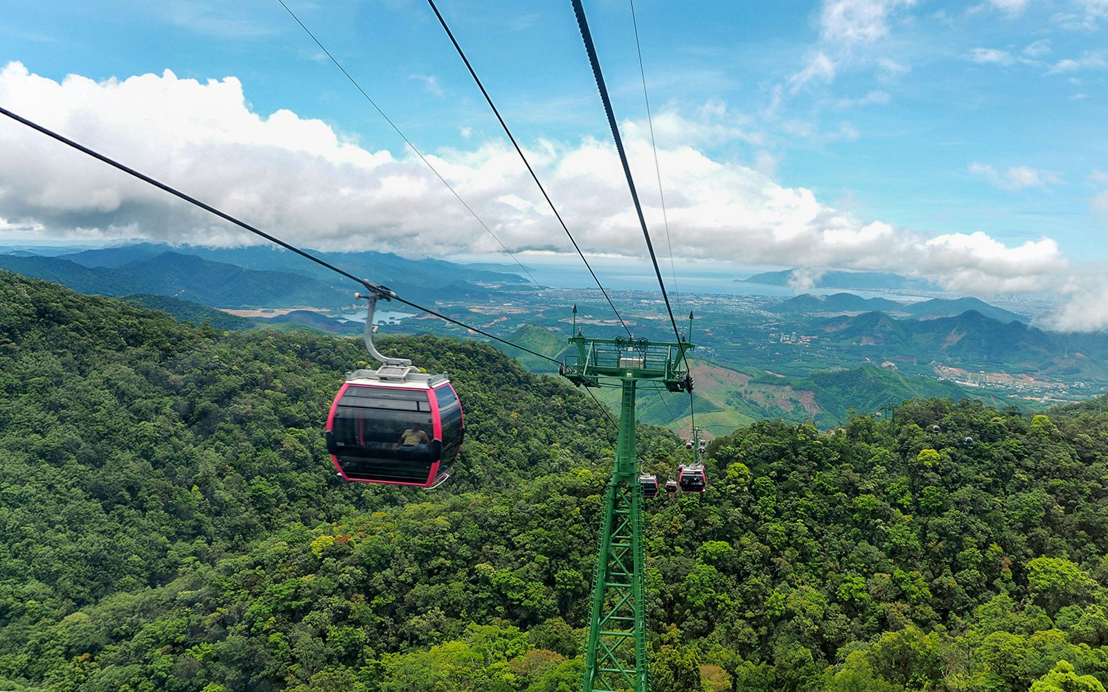 Cable car ascending Ba Na Hills with lush greenery and distant mountains in Da Nang, Vietnam.