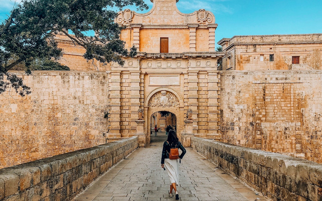 Person walking towards Mdina Gate, Malta, on a half-day tour including Dingli Cliffs and San Anton Gardens.
