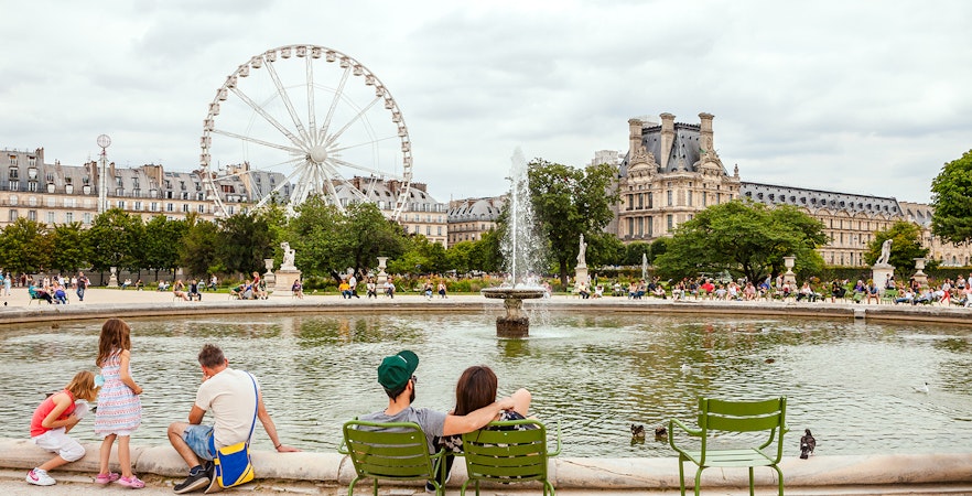People relaxing by the fountain in Tuileries Garden, Paris, with a Ferris wheel in the background.