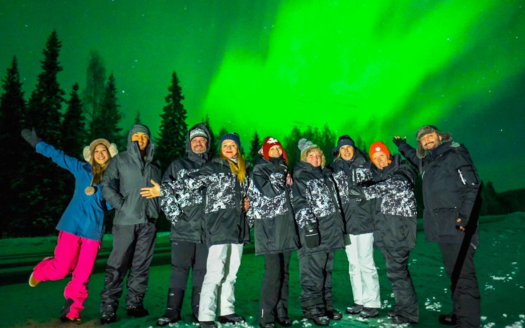 Group enjoying Northern Lights in Rovaniemi with vibrant green aurora overhead.