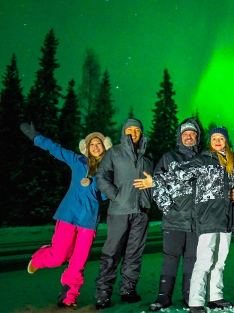 Group enjoying Northern Lights in Rovaniemi with vibrant green aurora overhead.