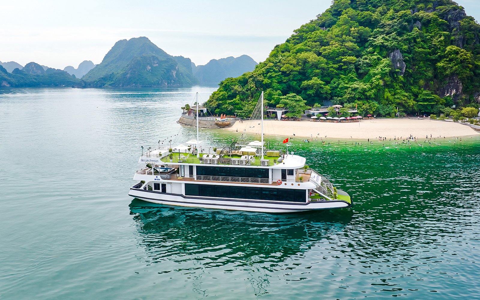 Cruise ship Hercules Premium near a scenic island with lush greenery and a sandy beach.
