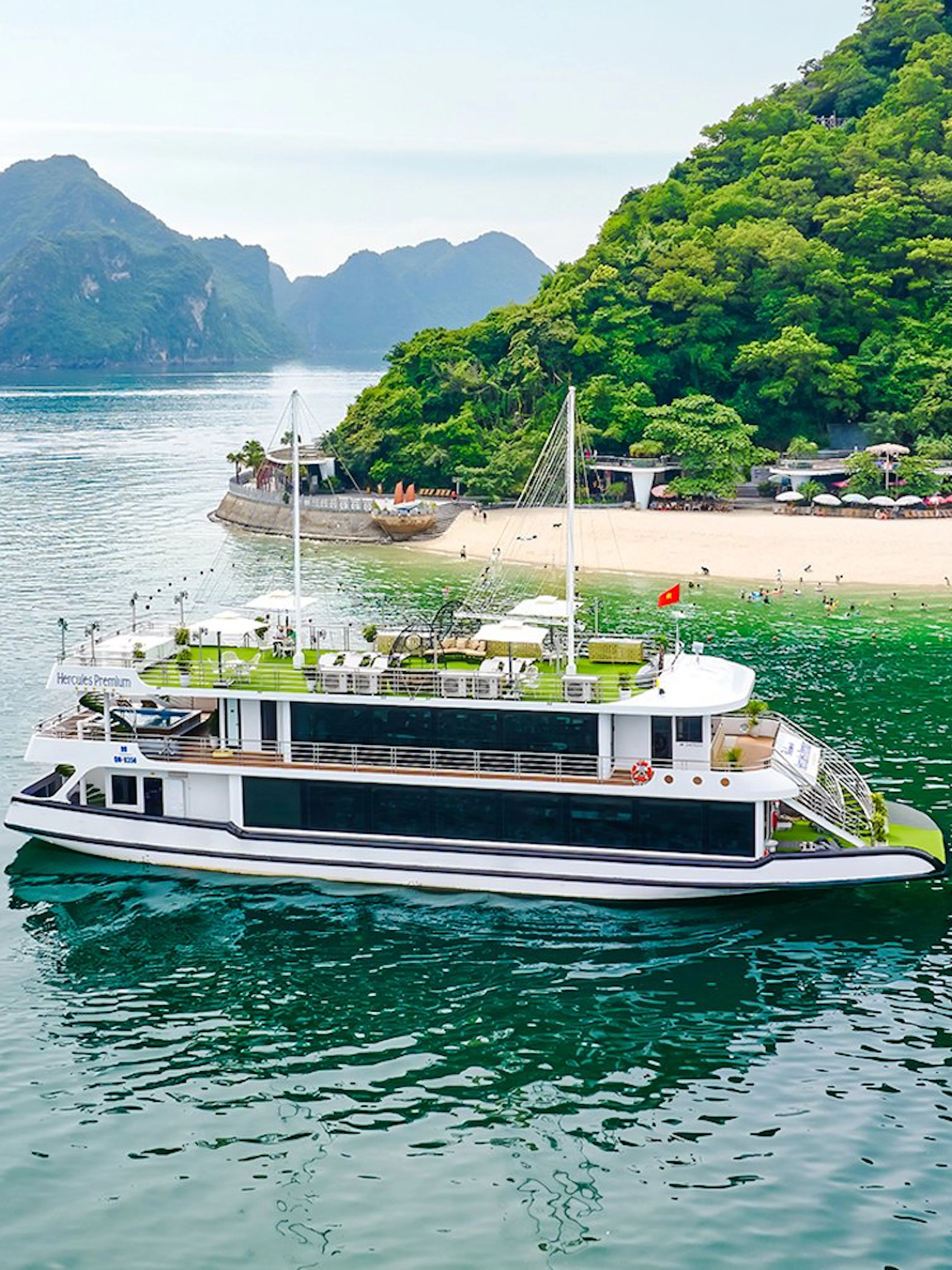 Cruise ship Hercules Premium near a scenic island with lush greenery and a sandy beach.