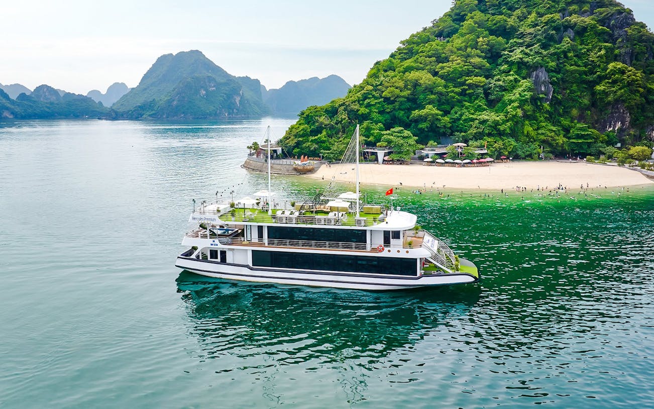 Cruise ship Hercules Premium near a scenic island with lush greenery and a sandy beach.