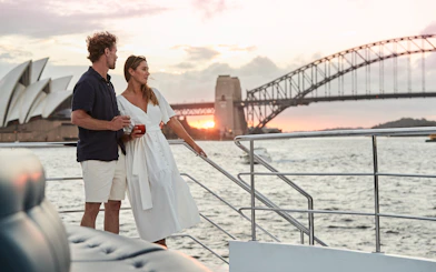 Couple enjoying sunset on Sydney Harbour dinner cruise with Opera House and Harbour Bridge in view.