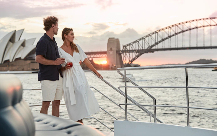 Couple enjoying sunset on Sydney Harbour dinner cruise with Opera House and Harbour Bridge in view.
