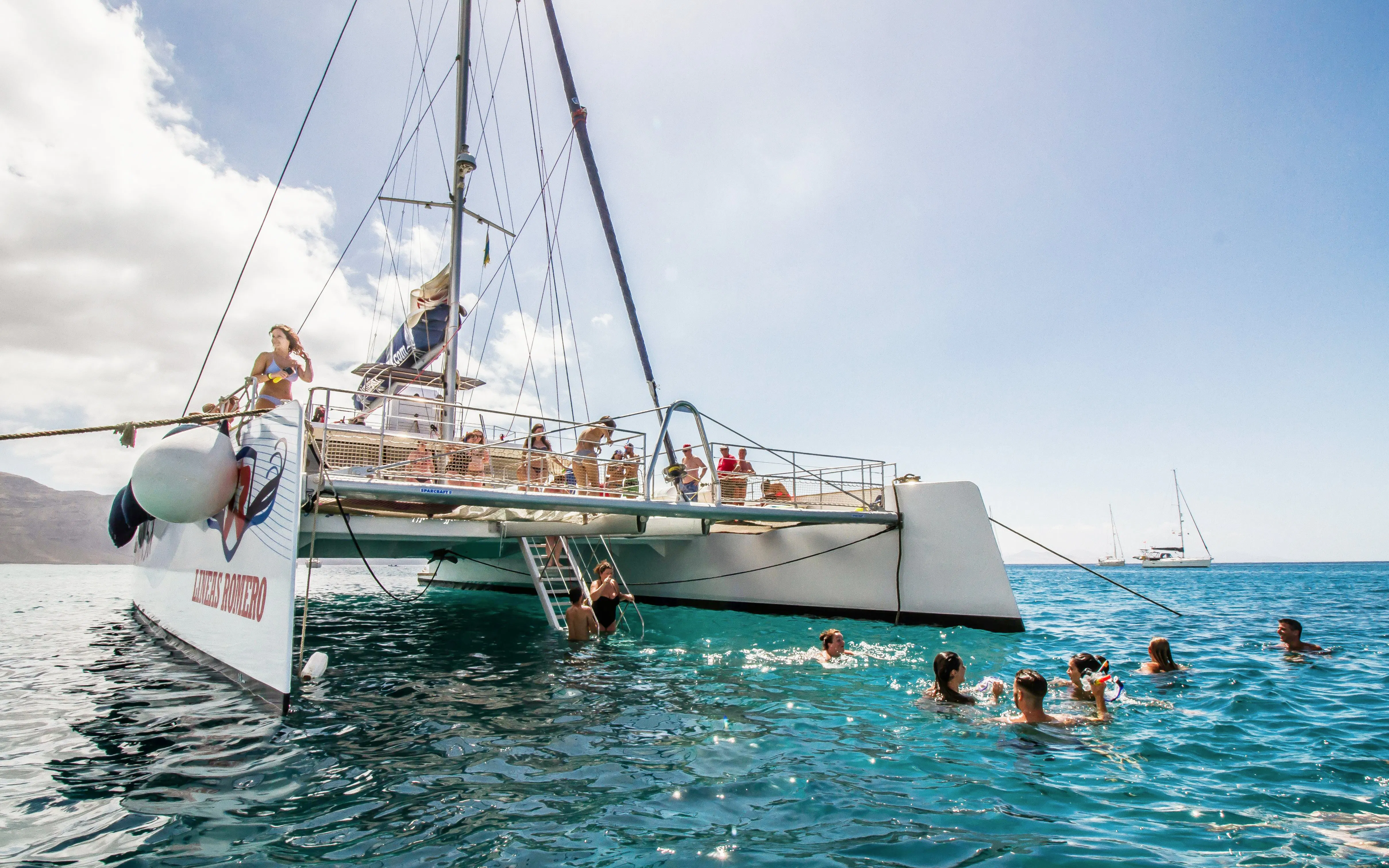 Catamaran anchored near La Graciosa Island with people swimming and relaxing on deck.
