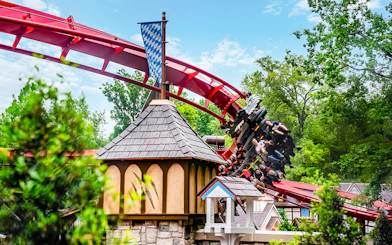 Roller coaster at Busch Gardens Williamsburg with riders on a red track near a Bavarian-style building.