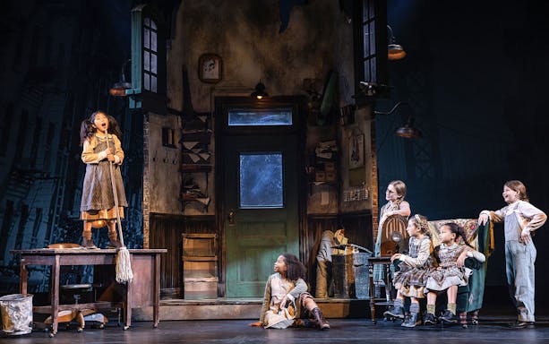 Children performing a scene from the musical "Annie" on stage.