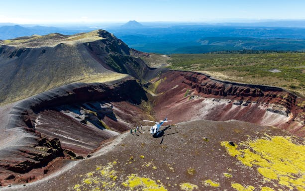 Helicopter landing on Mount Tarawera crater with tourists exploring volcanic landscape.