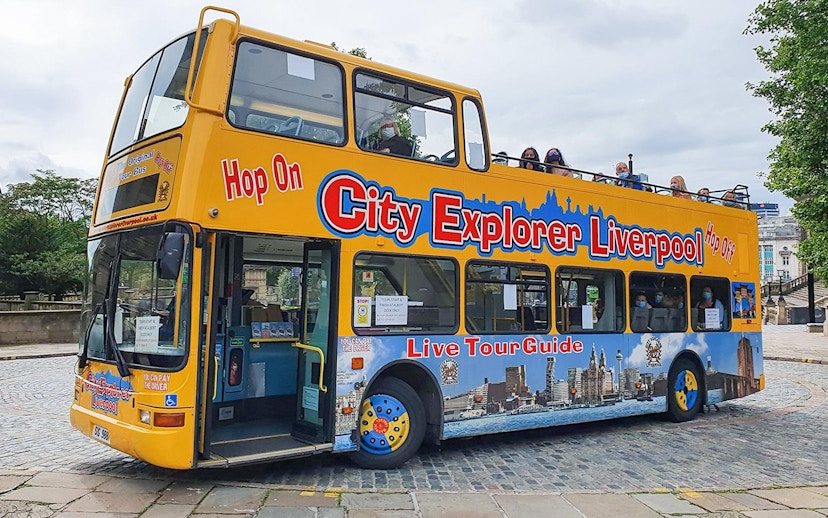 Open-top City Explorer Liverpool tour bus on cobblestone street.