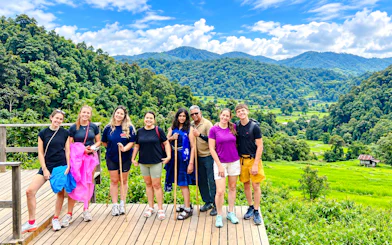 Group of tourists on a wooden deck with lush green hills in Doi Inthanon, Chiang Mai.