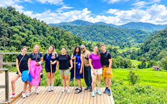 Group of tourists on a wooden deck with lush green hills in Doi Inthanon, Chiang Mai.