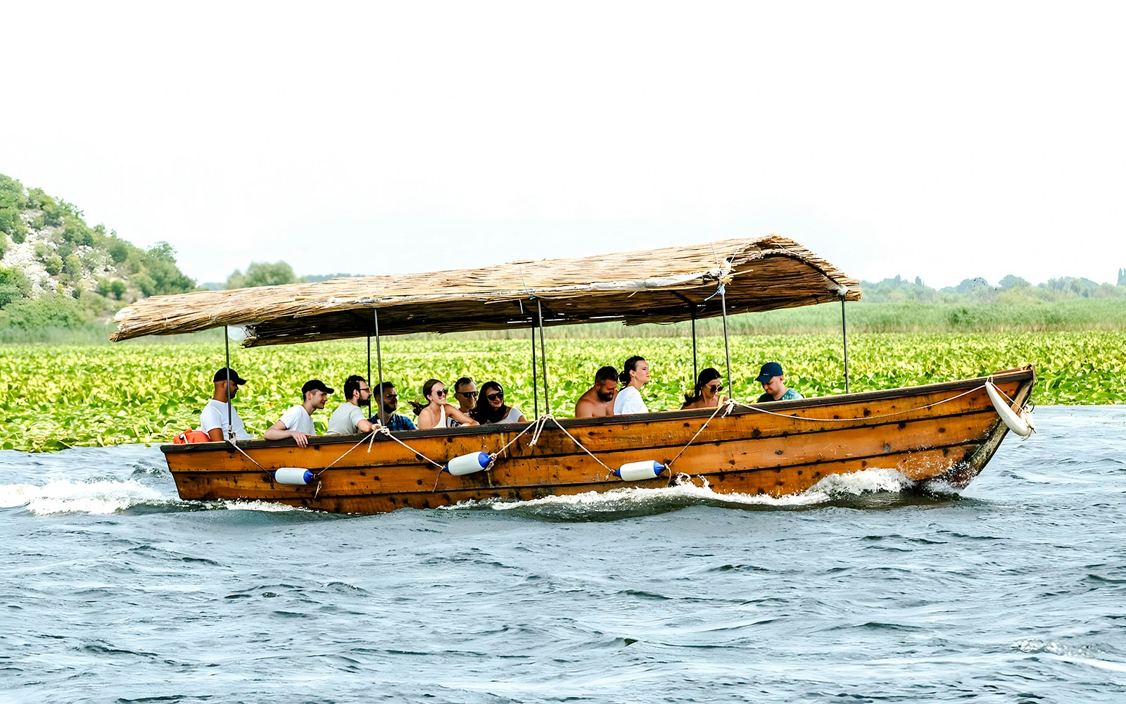 Guided sightseeing tour on a wooden boat at Lake Skadar with passengers enjoying the view.