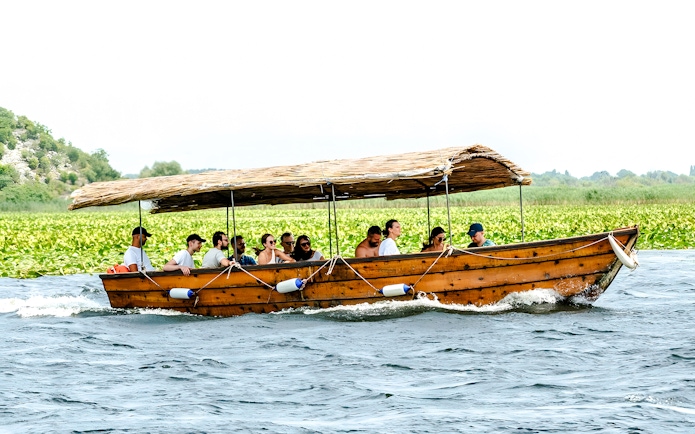 Guided sightseeing tour on a wooden boat at Lake Skadar with passengers enjoying the view.
