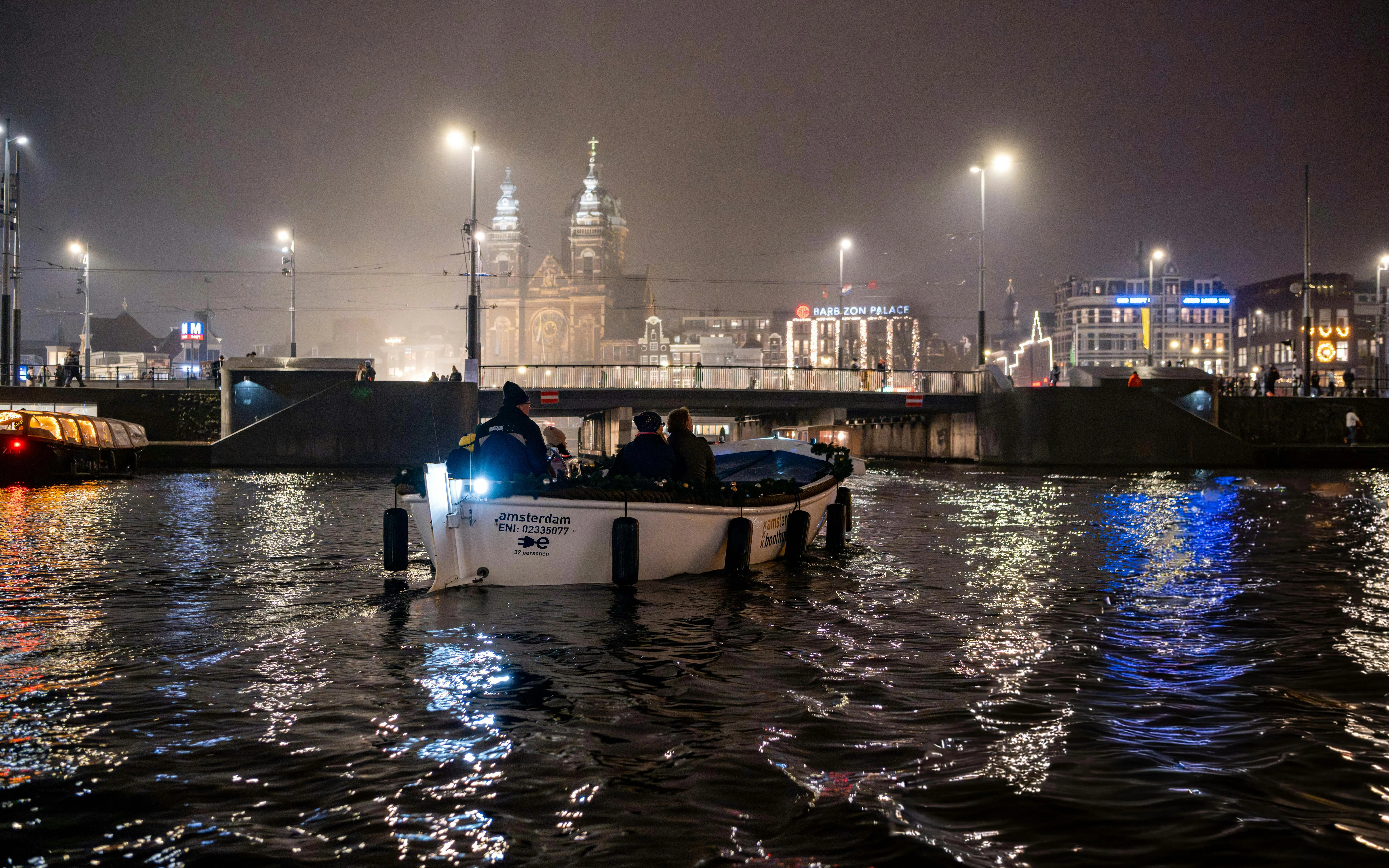 Boat tour during Amsterdam Light Festival with illuminated cityscape in the background.