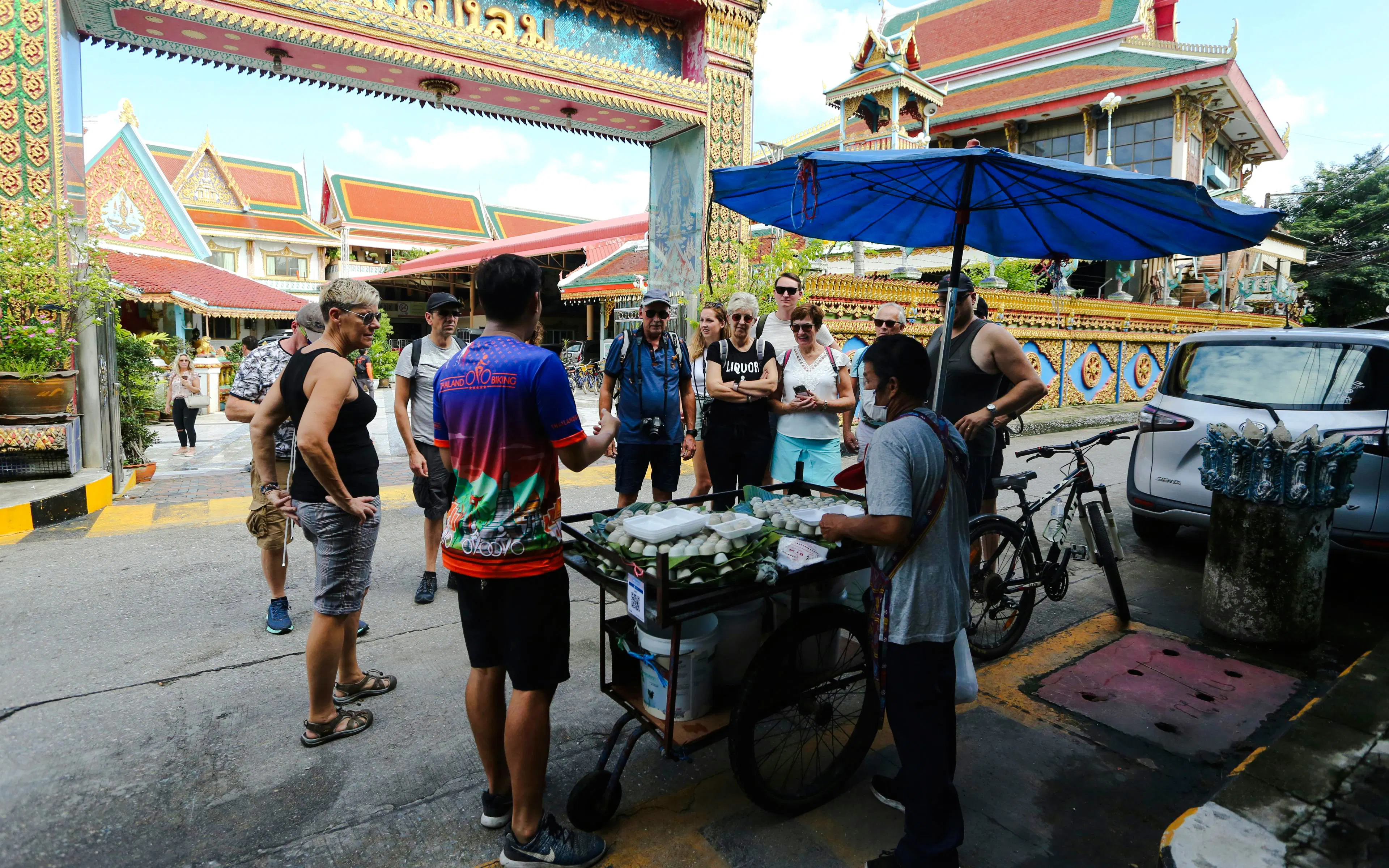 Tour group at a street food cart near a temple in Bangkok during city culture ride.