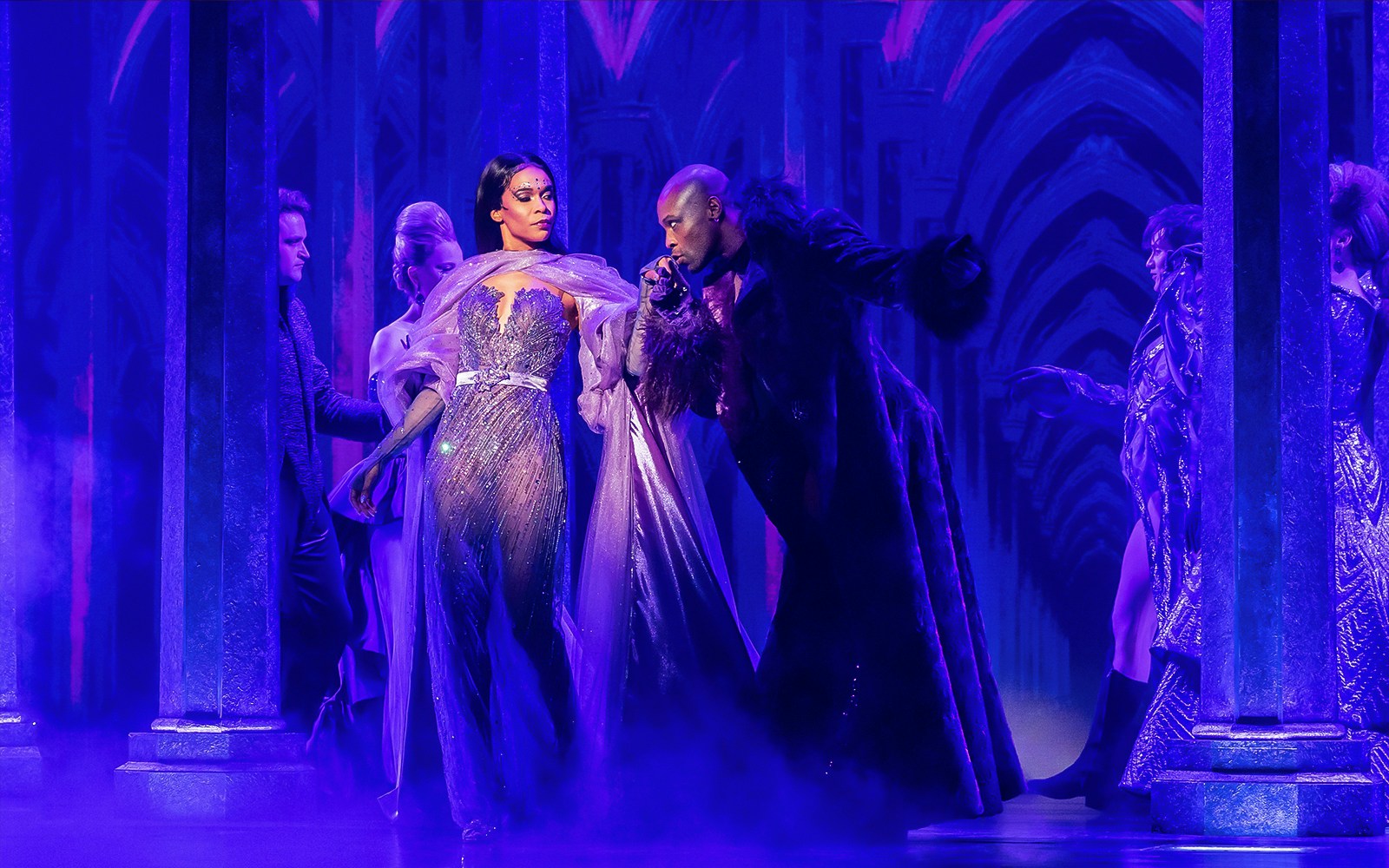 Performers in a theatrical scene from "Death Becomes Her" with dramatic lighting and costumes.