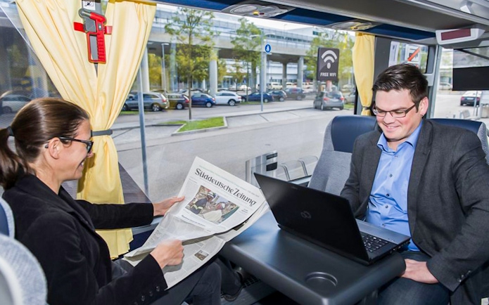 Passenger reading newspaper on airport transfer bus with free WiFi.