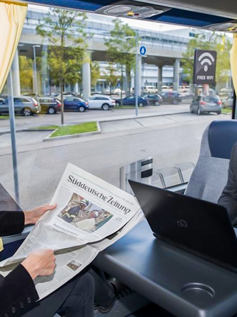 Passenger reading newspaper on airport transfer bus with free WiFi.