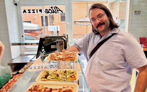 Man enjoying pizza slices at a pizzeria in Trastevere, Rome during a food tour.