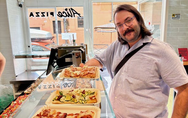 Man enjoying pizza slices at a pizzeria in Trastevere, Rome during a food tour.