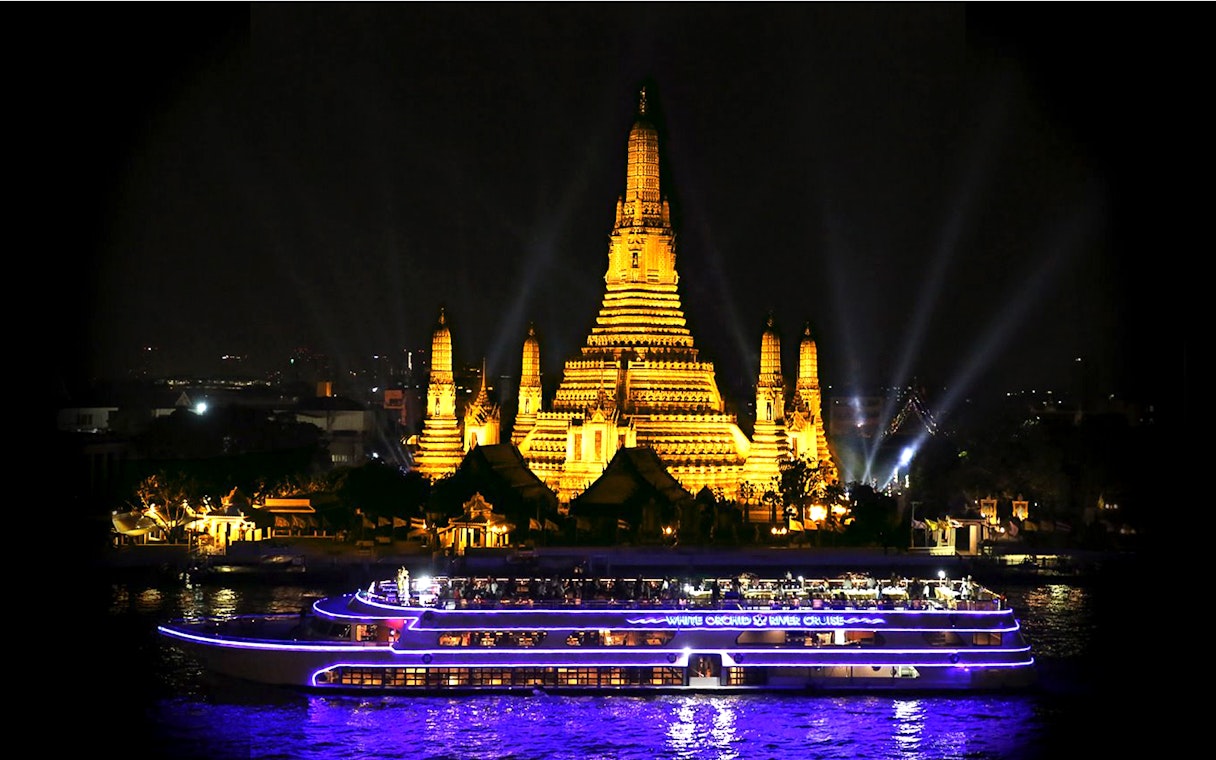 White Orchid River Cruise passing Wat Arun illuminated at night in Bangkok.