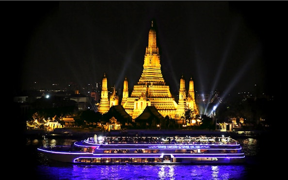 White Orchid River Cruise passing Wat Arun illuminated at night in Bangkok.