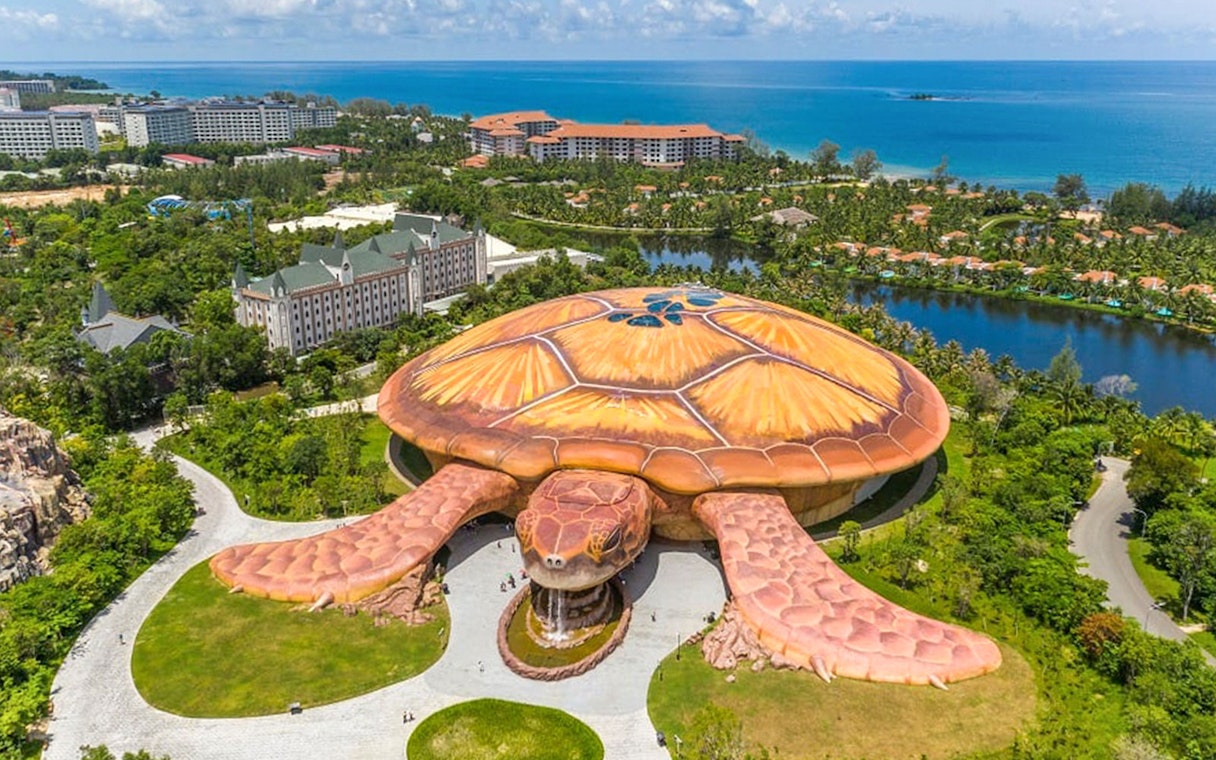 Aerial view of turtle-shaped building at VinWonders, Phu Quoc, with ocean in background.