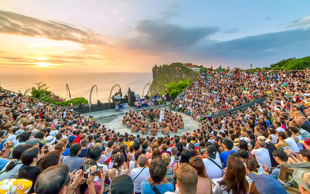 Crowd watching Kecak dance performance at Uluwatu Temple, Bali, during sunset.