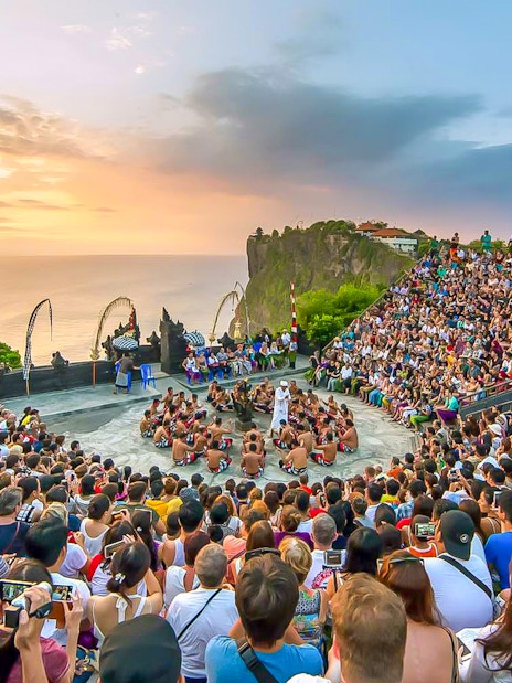 Crowd watching Kecak dance performance at Uluwatu Temple, Bali, during sunset.