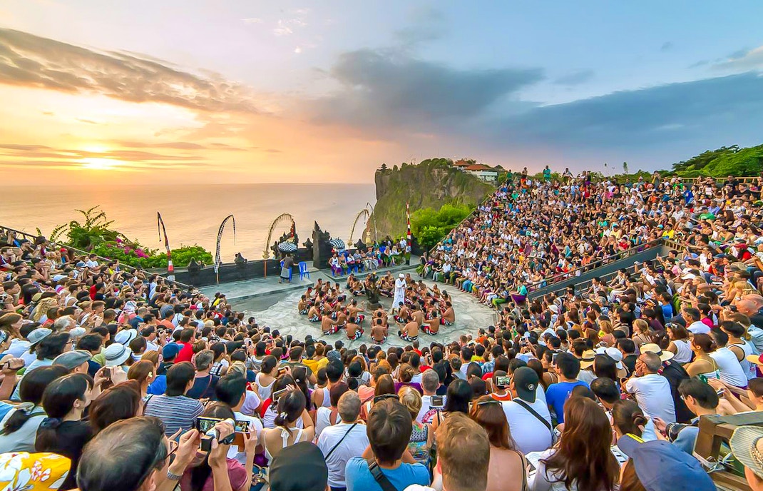 Crowd watching Kecak dance performance at Uluwatu Temple, Bali, during sunset.