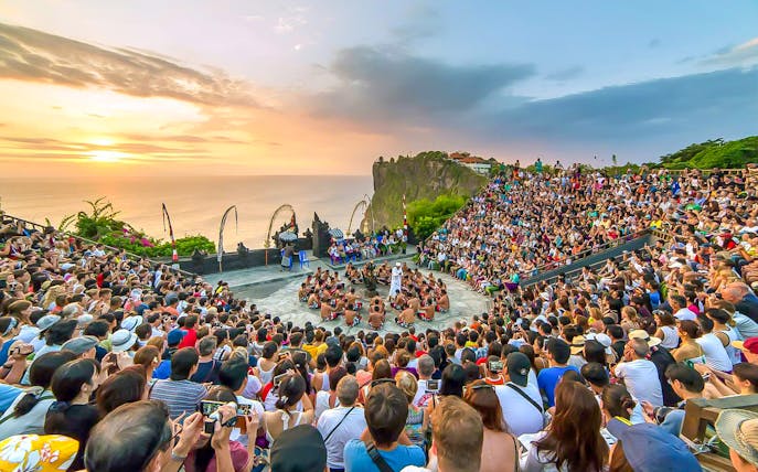 Crowd watching Kecak dance performance at Uluwatu Temple, Bali, during sunset.