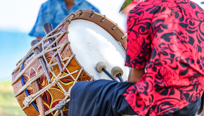 Man playing Pahu drum at a Hawaiian luau.