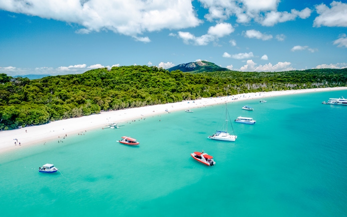 Aerial view of boats near Whitehaven Beach, Whitsundays, with lush greenery and clear blue water.