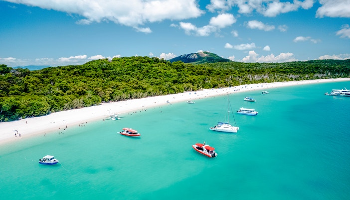Aerial view of boats near Whitehaven Beach, Whitsundays, with lush greenery and clear blue water.