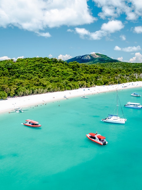 Aerial view of boats near Whitehaven Beach, Whitsundays, with lush greenery and clear blue water.