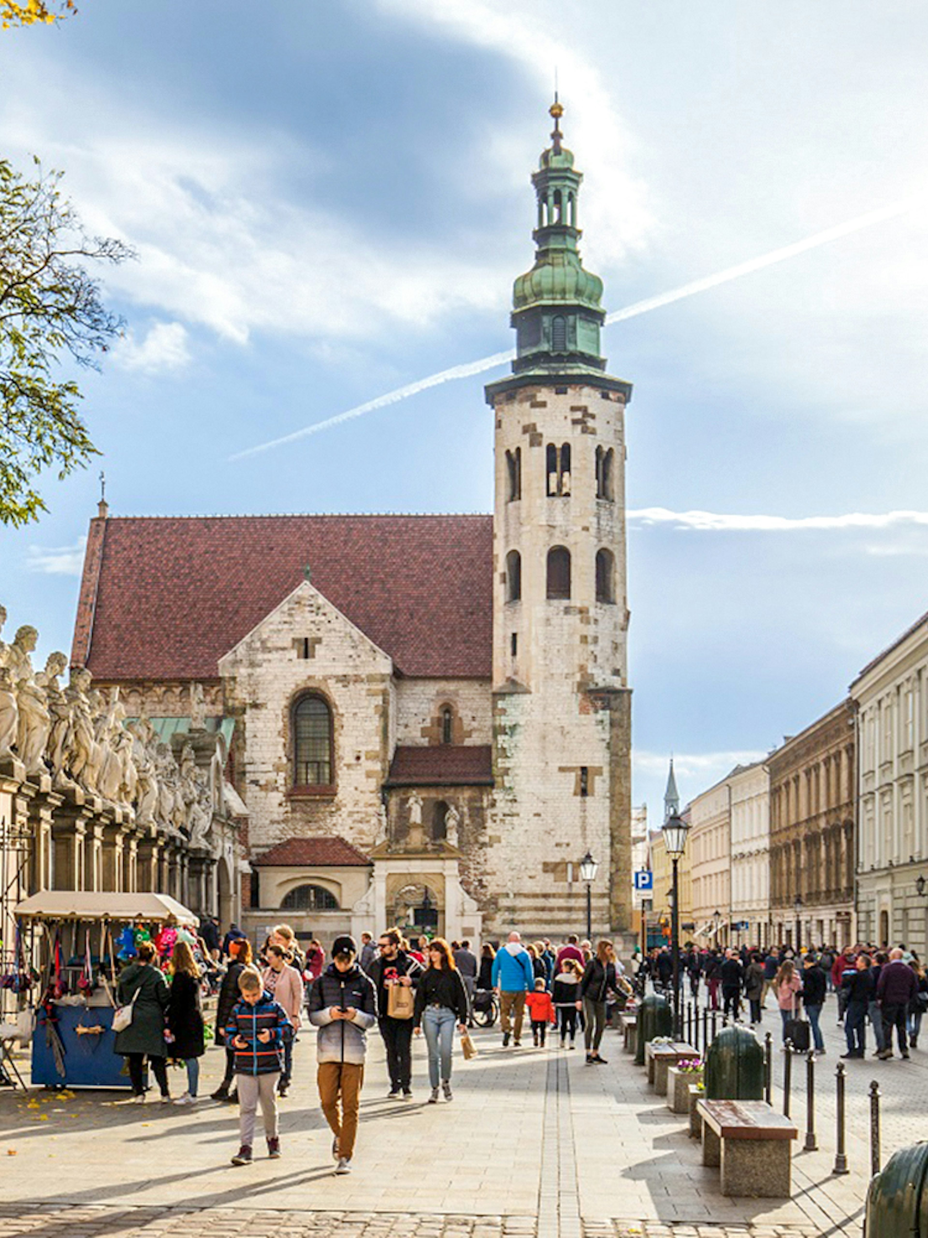 Tourists walking in Krakow Old Town near historic church and street vendors.