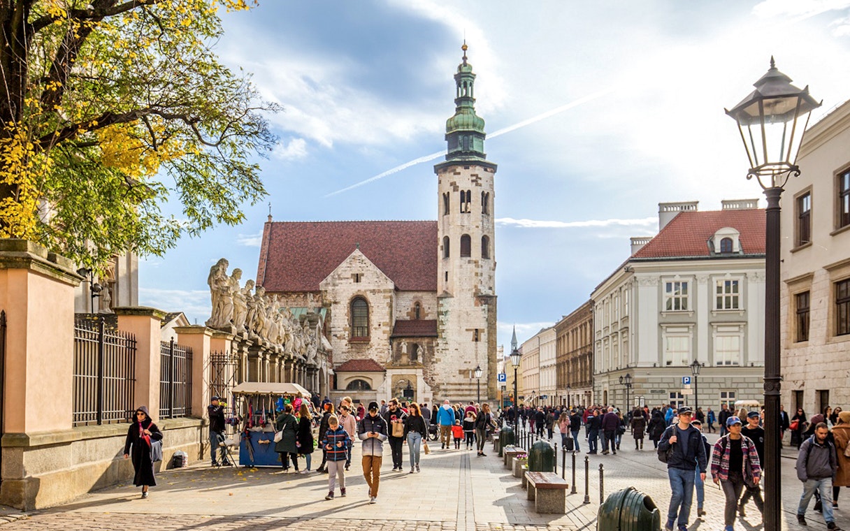 Tourists walking in Krakow Old Town near historic church and street vendors.