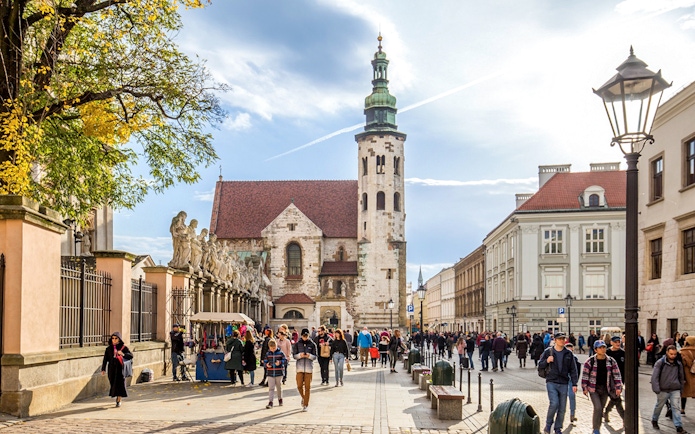 Tourists walking in Krakow Old Town near historic church and street vendors.