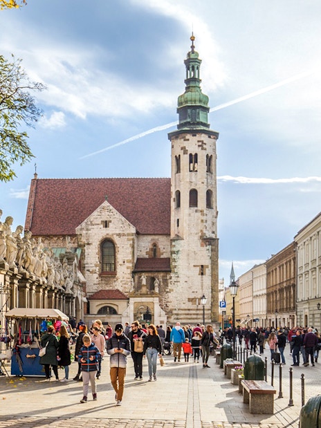 Tourists walking in Krakow Old Town near historic church and street vendors.