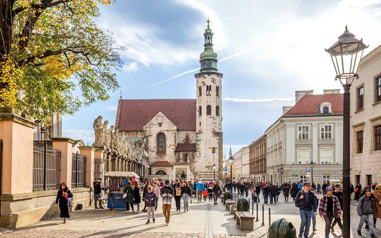 Tourists walking in Krakow Old Town near historic church and street vendors.