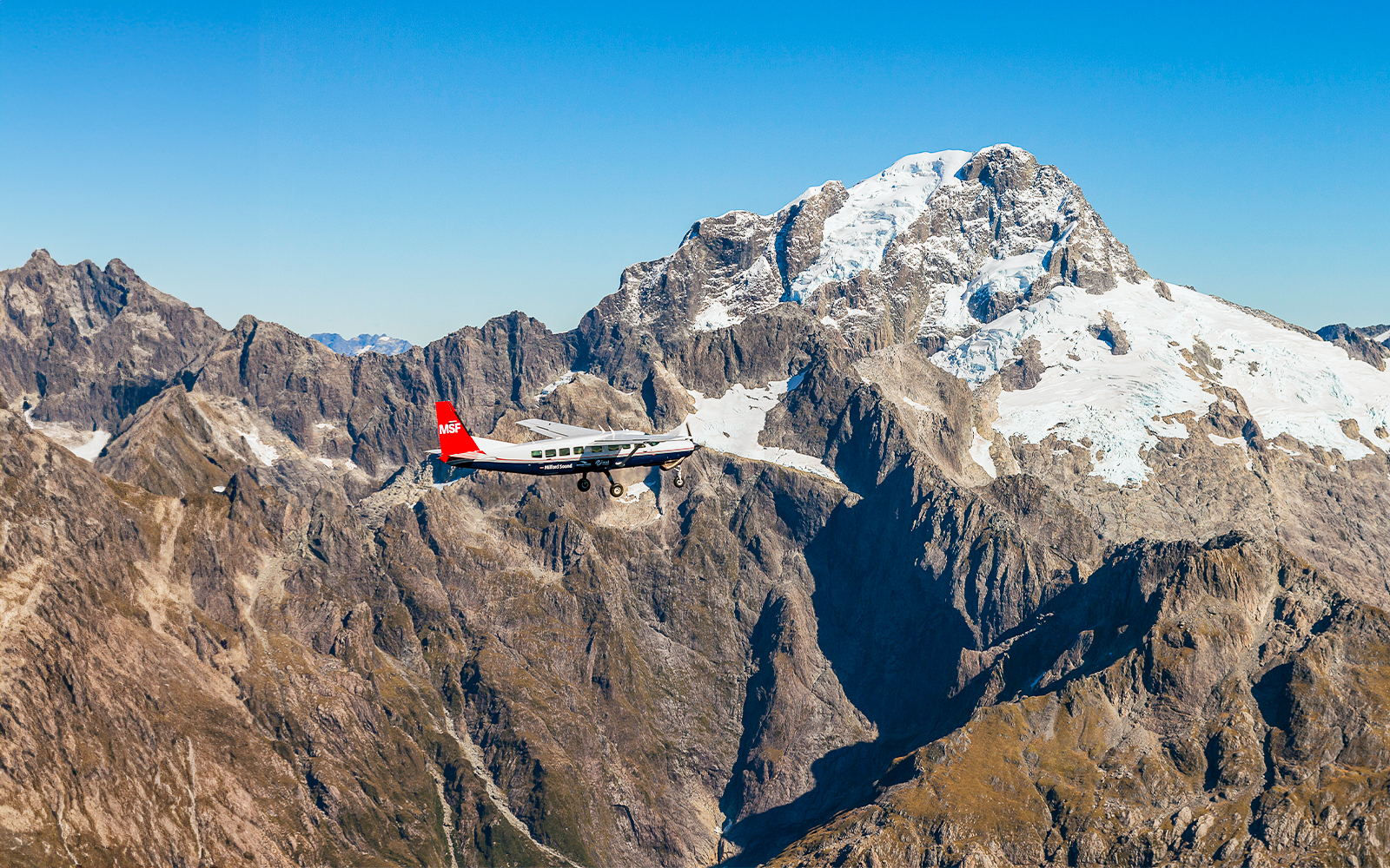 Small plane flying over snow-capped mountains during Milford Sound scenic flyover from Queenstown.