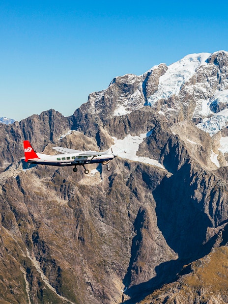 Small plane flying over snow-capped mountains during Milford Sound scenic flyover from Queenstown.