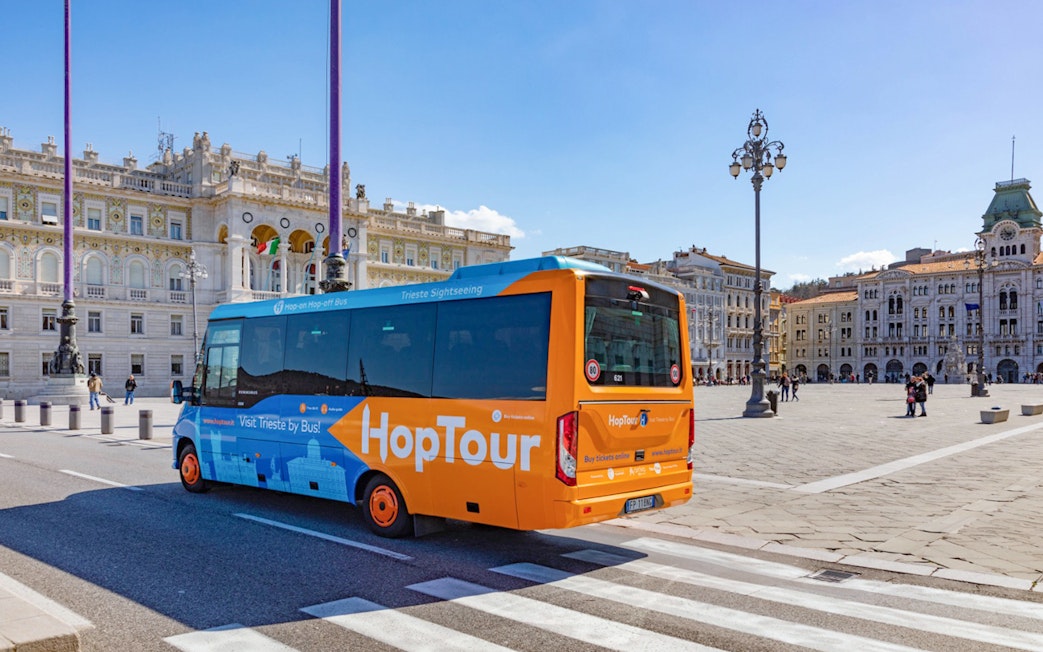 Trieste hop-on hop-off bus near Piazza Unità d'Italia with city landmarks.