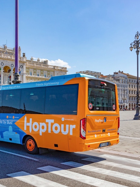 Trieste hop-on hop-off bus near Piazza Unità d'Italia with city landmarks.