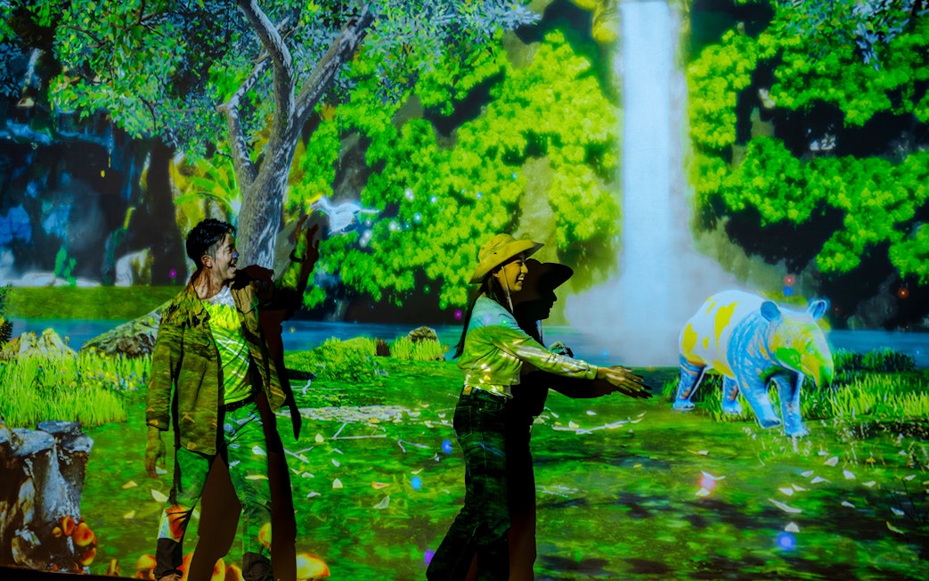 Tourists interacting with colorful digital displays in Enchanted Forest exhibit.