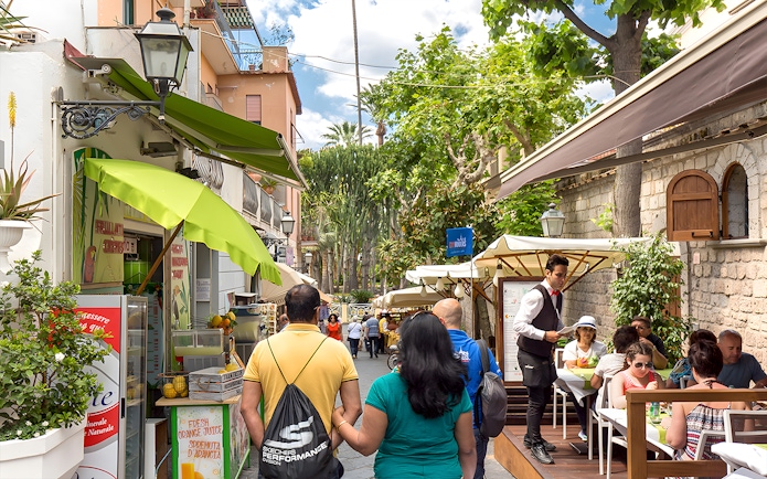 Street cafe in Positano with tourists dining and exploring, part of a guided day trip from Rome.